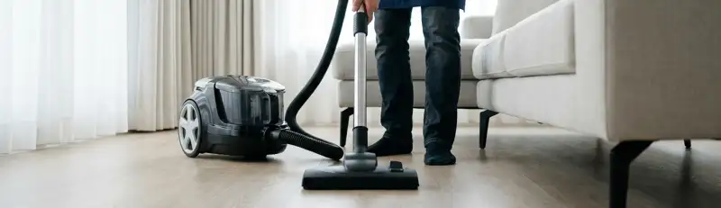 Professional house cleaner vacuuming a living room floor with a canister vacuum cleaner, Toledo, OH.
