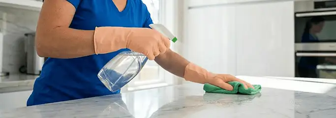 Maid service worker spraying and wiping a kitchen countertop with a microfiber cloth for sanitizing, Toledo, OH.