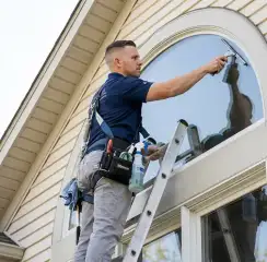 Professional window cleaner on a ladder using a squeegee to clean an exterior arched window, Toledo, OH.