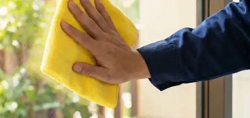 House cleaner wiping a glass window with a yellow microfiber cloth for streak-free cleaning, Toledo, OH.